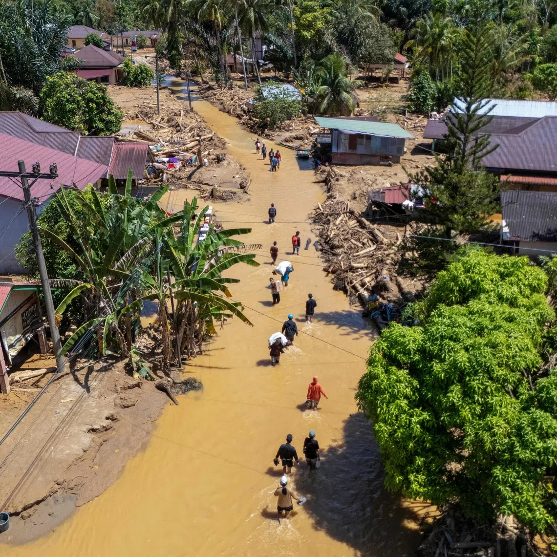 Villagers wading through the mudflow to find a shelter in the aftermath of flash floods in Tukka village, Central Tapanuli, North Sumatra province, on Dec 3.