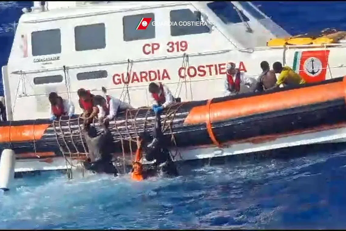 This handout photograph taken on August 5, 2023 by Italian Coastguard (Guardia Costeria) and released on August 6, 2023, shows rescuers helping migrants to board a rescue boat during operations that took place south of Lampedusa, rescuing 57 migrants and also recovering the lifeless bodies of a woman and a minor on board. At least 30 migrants are missing following two shipwrecks off the Italian island of Lampedusa, according to survivor testimony, as rescuers on August 26, 2023 winched to safety 34 others stranded on the rocks by rough seas. (Photo by Italian Coastguard / GUARDIA COSTIERA / AFP) / -----EDITORS NOTE --- RESTRICTED TO EDITORIAL USE - MANDATORY CREDIT "AFP PHOTO /HANDOUT/GUARDIA COSTERIA " - NO MARKETING - NO ADVERTISING CAMPAIGNS - DISTRIBUTED AS A SERVICE TO CLIENTS  - NO ARCHIVES