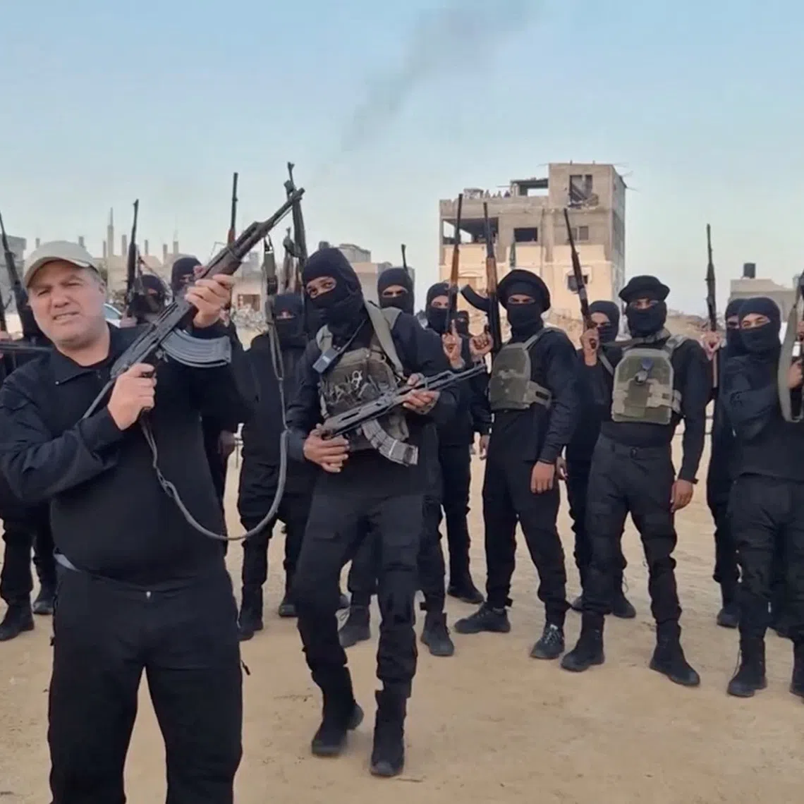 The head of an anti-Hamas faction, Hussam Alastal, fires a weapon in the air as he is surrounded by masked gunmen, in an Israeli-held area in Khan Younis, in the southern Gaza Strip, in this screenshot taken from a video released November 21, 2025. Hussam Alastal/via REUTERS
