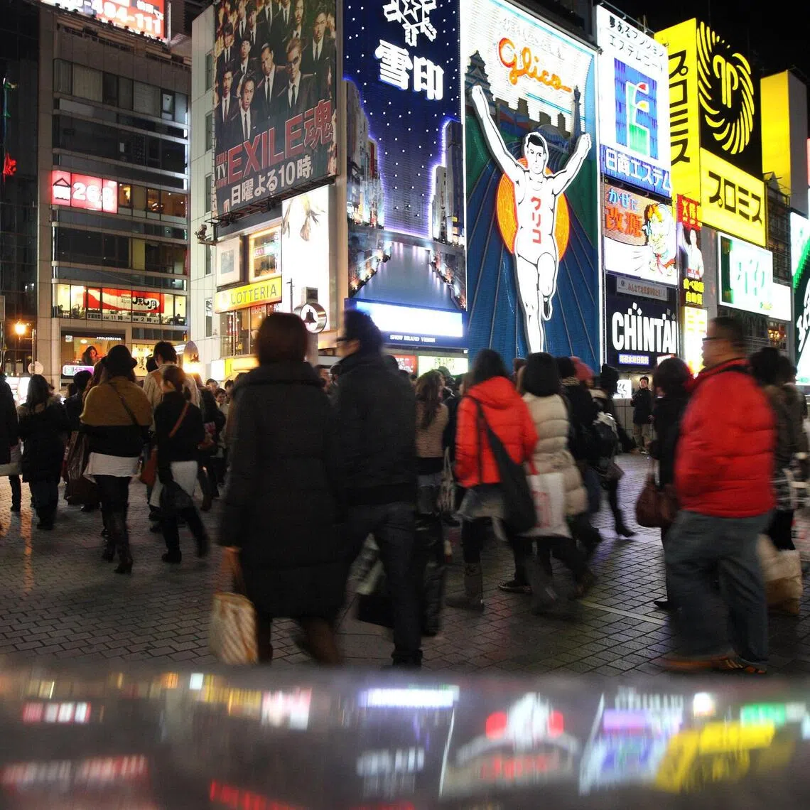 Pedestrians walk in front of advertisements in the Dotonbori area of Osaka, Japan, on Monday, Jan. 3, 2011. The wider Osaka metropolitan area, with a population of 11 million, is Japan's largest after Tokyo with 35 million , according to data compiled by the United Nations. Photographer: Tomohiro Ohsumi/Bloomberg