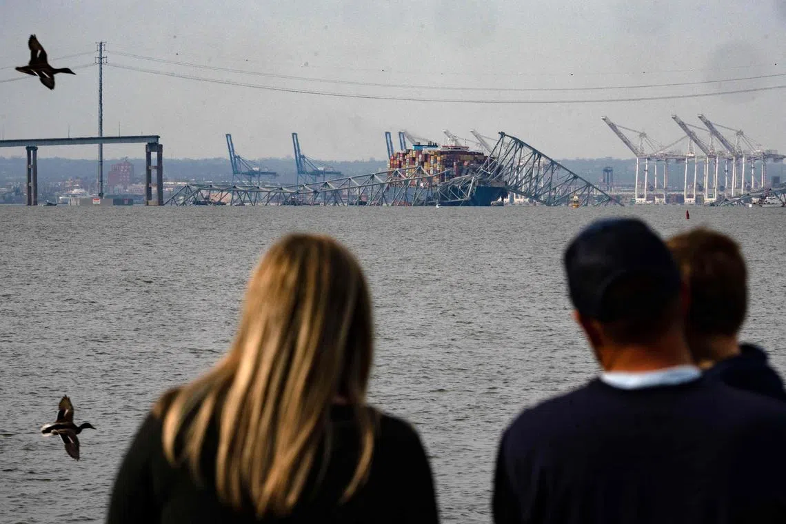 A family looking at the steel frame of the Francis Scott Key Bridge sitting on top of the container ship Dali after the bridge collapsed in Baltimore, Maryland, on March 26, 2024. 
