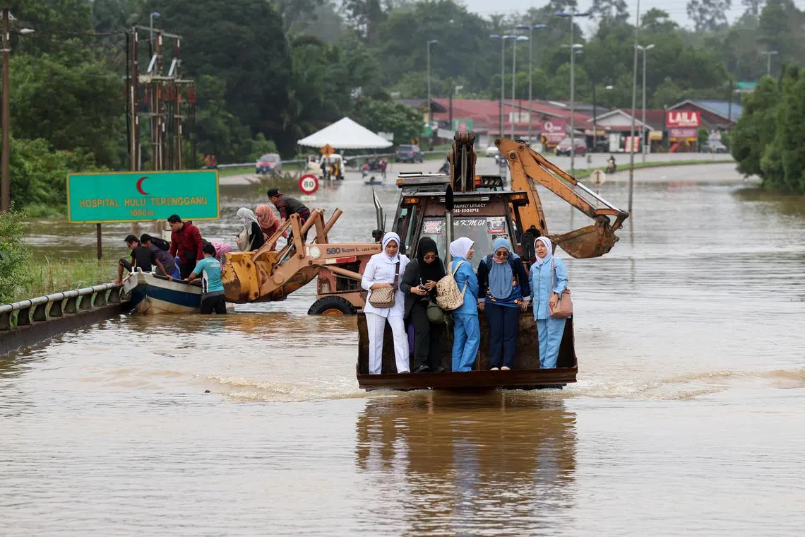 KUALA BERANG - Staff from Hospital Hulu Terengganu being lifted by an excavator before being transferred to a boat on their way to work on Dec 27, as roads became unpassable.