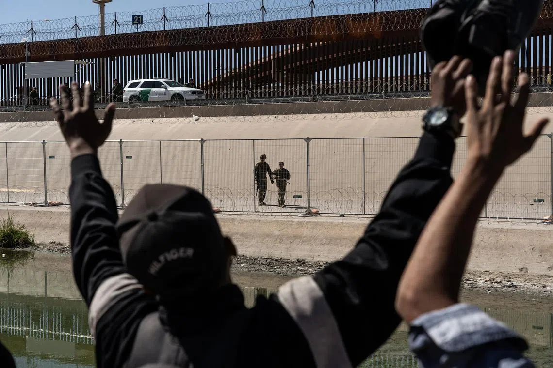 Asylum seekers from Venezuela look over towards US National Guardsmen from the Mexican side of the border.