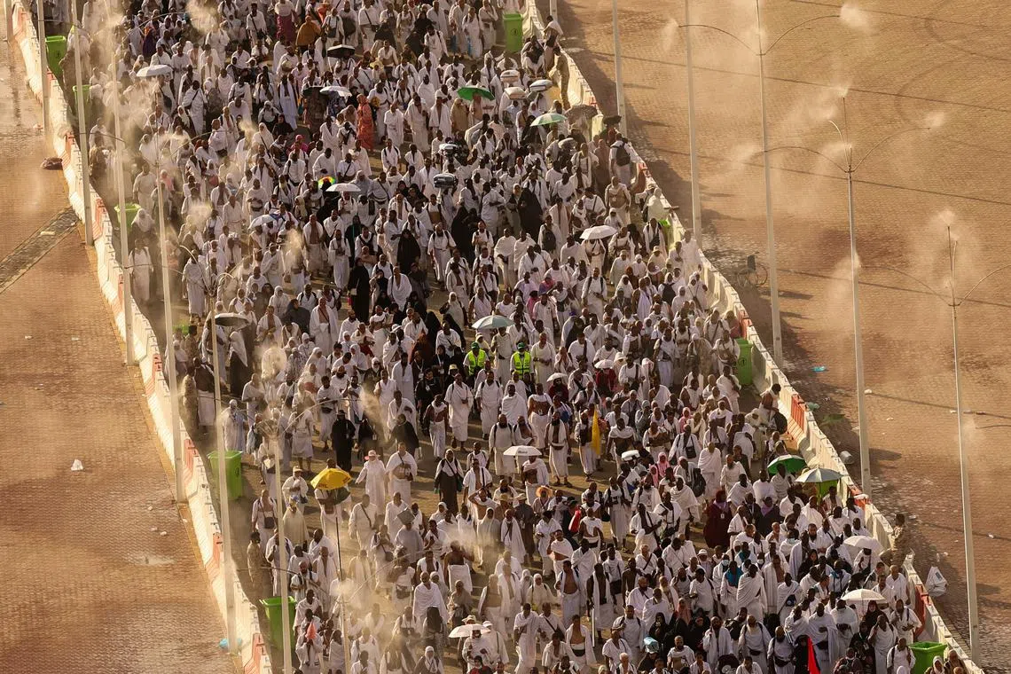 Pilgrims walk under mist dispensers during the annual hajj pilgrimage in Mina on June 16, 2024.
