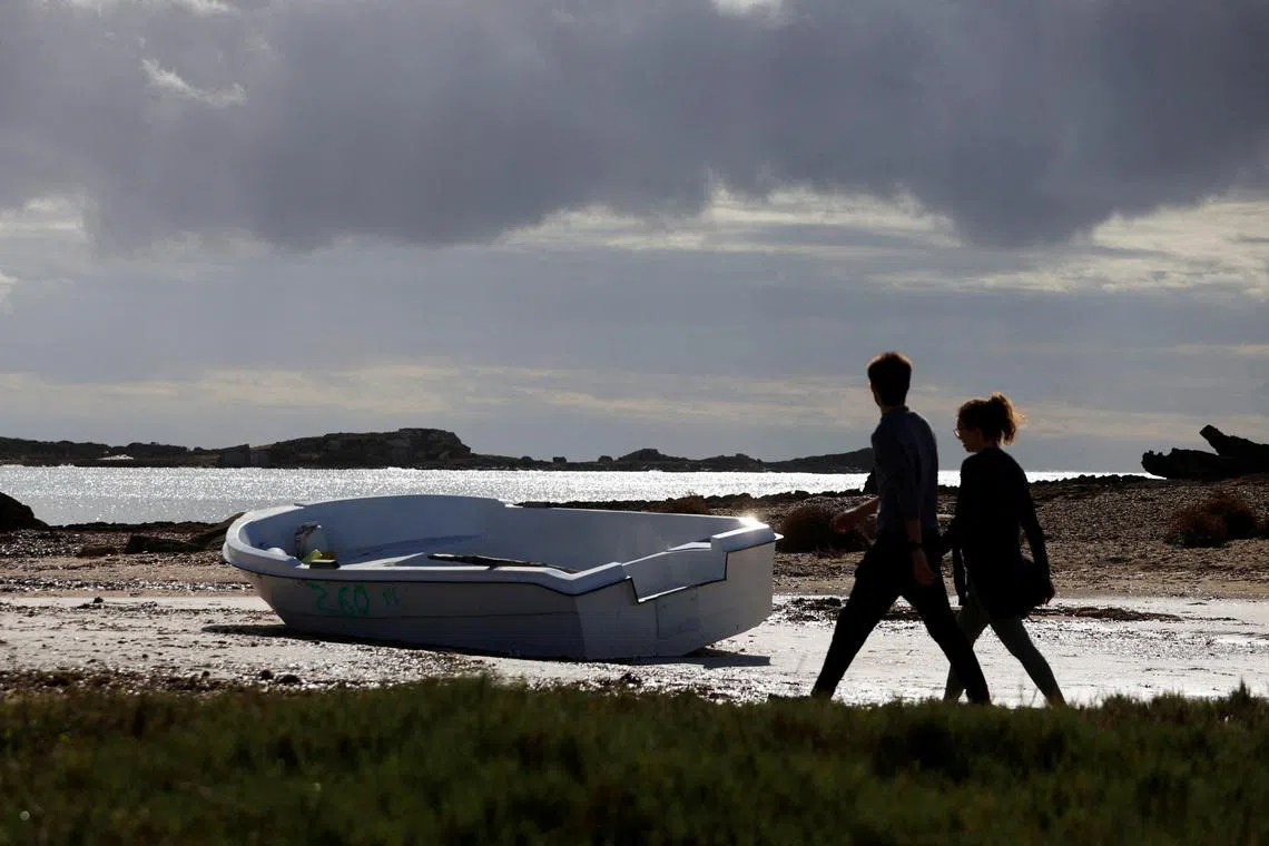 FILE PHOTO: People walk next to a discarded boat used by migrants to reach Mallorca rests on Es Caragol beach in the south of the Balearic island, in Santanyi, Mallorca, Spain, November 20, 2025. REUTERS/Francisco Ubilla/File Photo