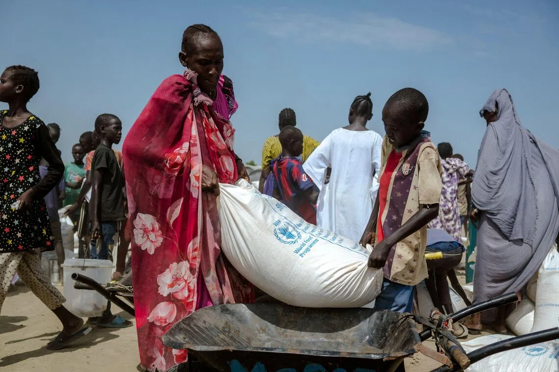 A mother and son lifting a heavy bag of maize into their wheelbarrow at a displaced persons camp in South Sudan, on Nov 6.