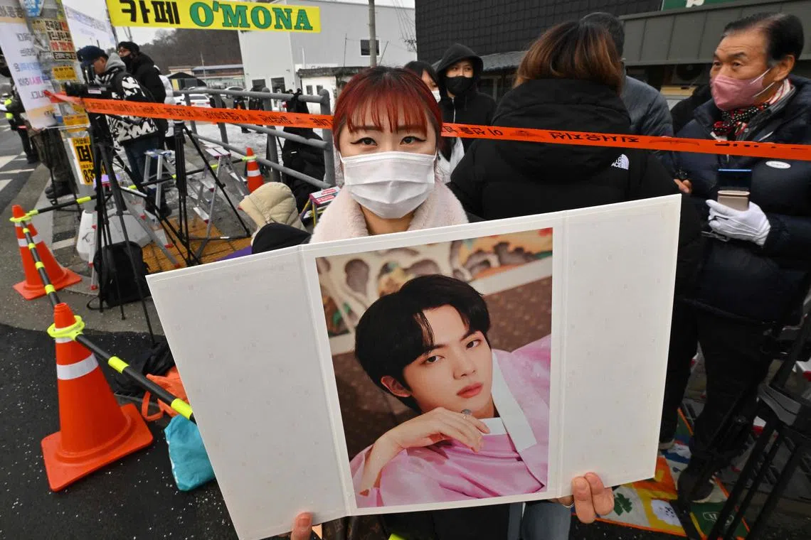 A fan holds a picture of BTS singer Jin in front of a military training unit in Yeoncheon, South Korea, on Dec 13, 2022. 