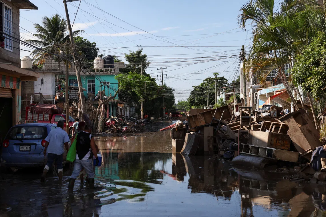 People wading through muddy floodwater after a river overflowed following torrential rains, in Poza Rica, Mexico, on October 15, 2025. 