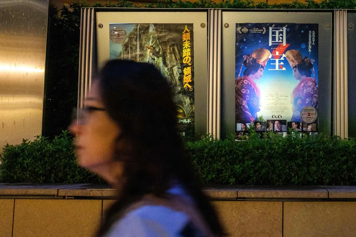 A woman walks past the poster of Japanese movie "Kokuho" (R) outside a cinema in Tokyo's Roppongi district.