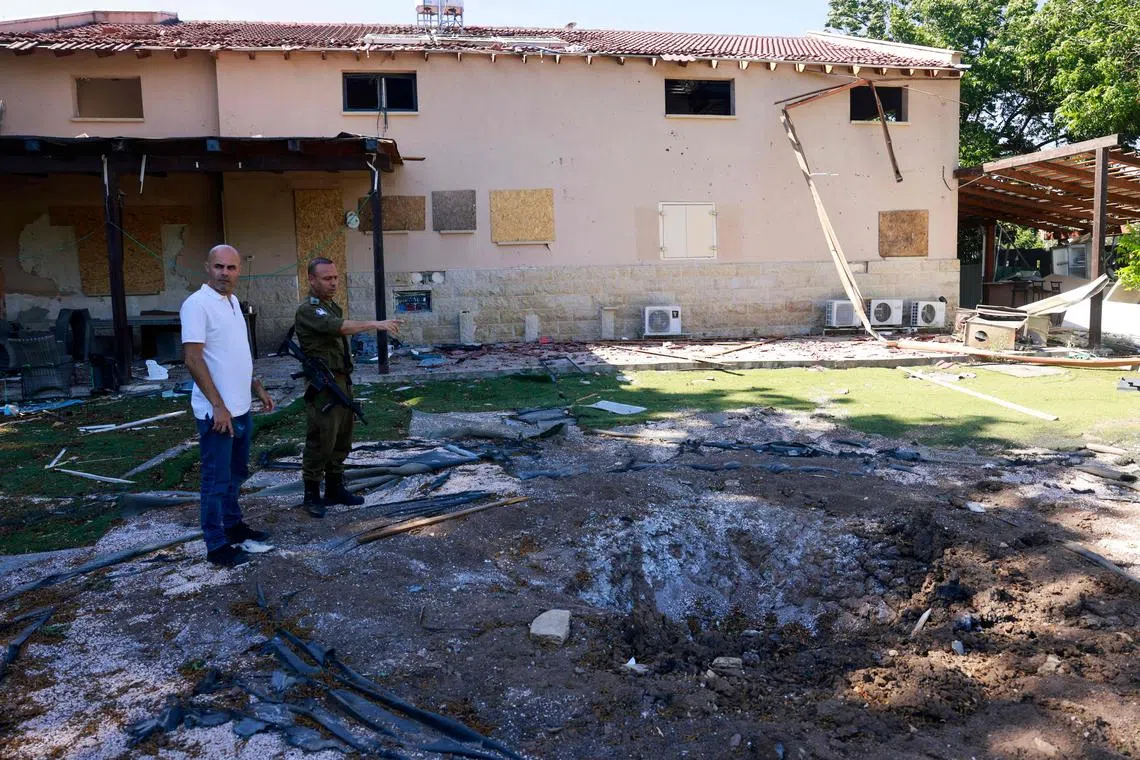 An Israeli soldier and a man check a crater on the ground at a house that was hit by a Hezbollah rocket in Kiryat Shmona.