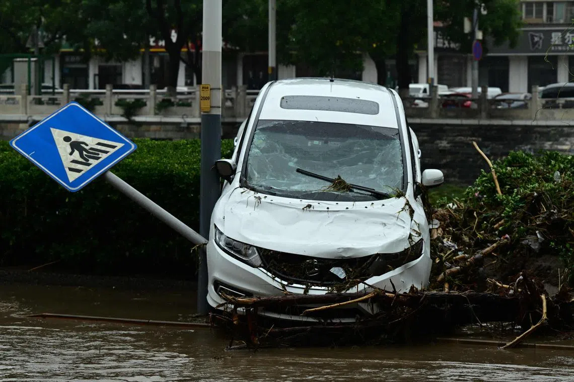 A damaged car is seen on the side of the road after heavy rains in Mentougou district in Beijing on August 1, 2023. At least 11 people are dead and 27 missing after heavy rains lashed Beijing, state media said on August 1, in downpours that have submerged roads and deluged neighbourhoods with mud. (Photo by Pedro PARDO / AFP)