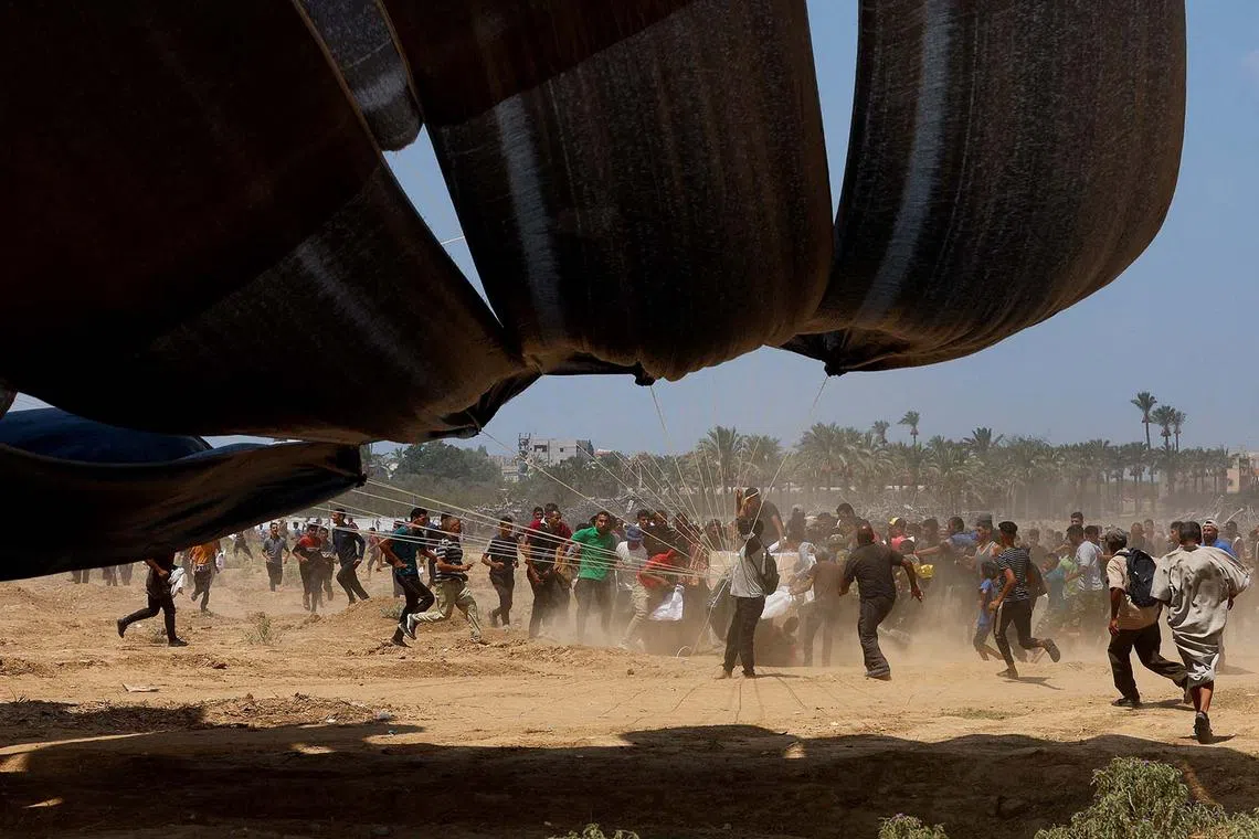 Palestinians running towards airdropped aid packages, in Deir Al-Balah, in the central Gaza Strip, Aug 18, 2025. 