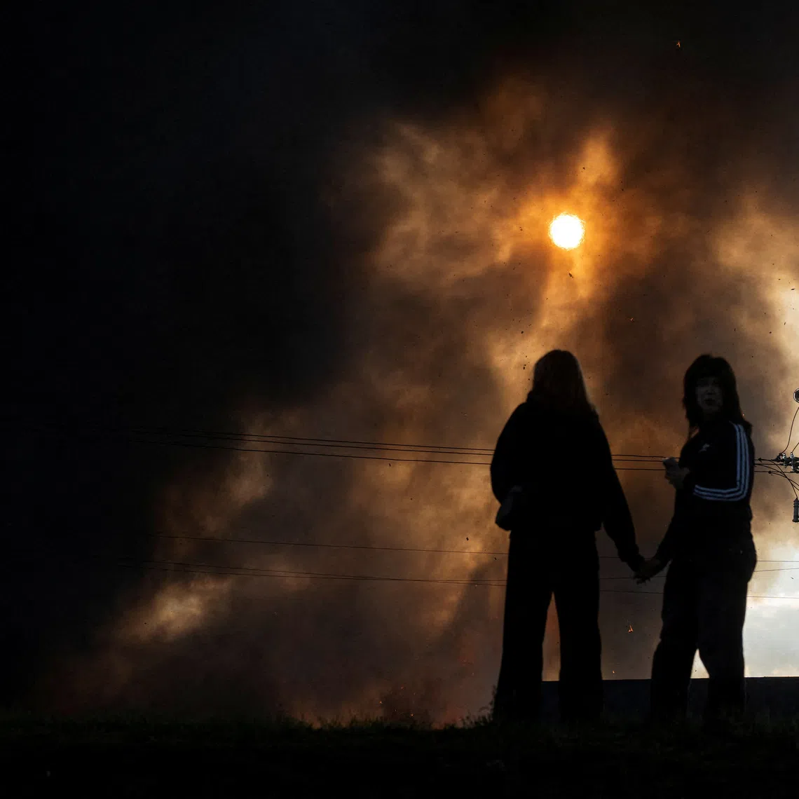 Residents hold hands as smoke rises over a warehouse, which was hit by a Russian drone strike, amid Russia's attack on Ukraine, in Kyiv region, Ukraine, September 20, 2026. REUTERS/Serhii Korovainyi