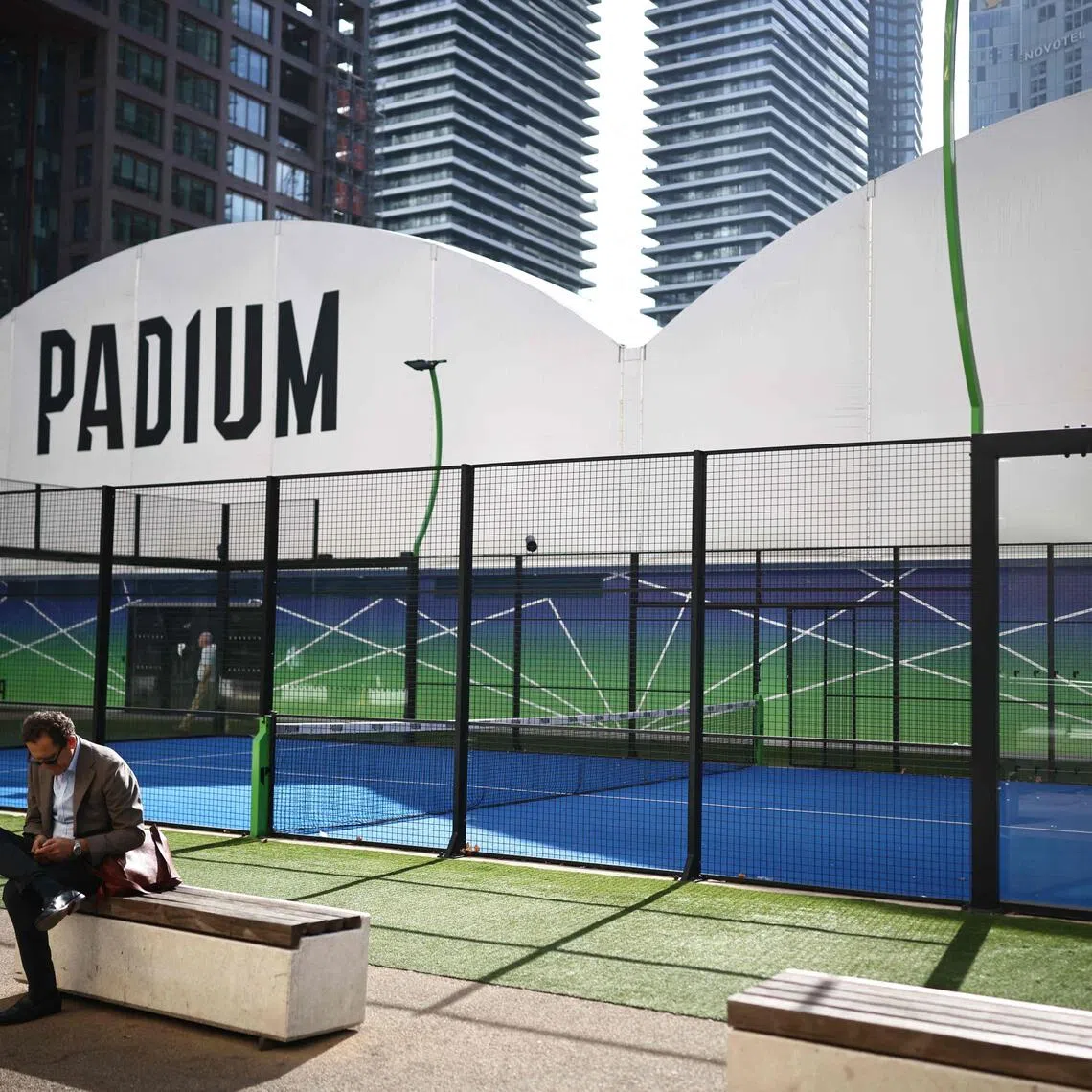 A person relaxes beside a padel court in east London on October 6, 2026. The recent growth in the UK of padel - a cross between tennis and squash played by doubles teams on courts enclosed by glass or wire - has sparked friction in some places, most notably London, where several sites with new or proposed courts have provoked pushback from local communities. (Photo by Henry NICHOLLS / AFP)