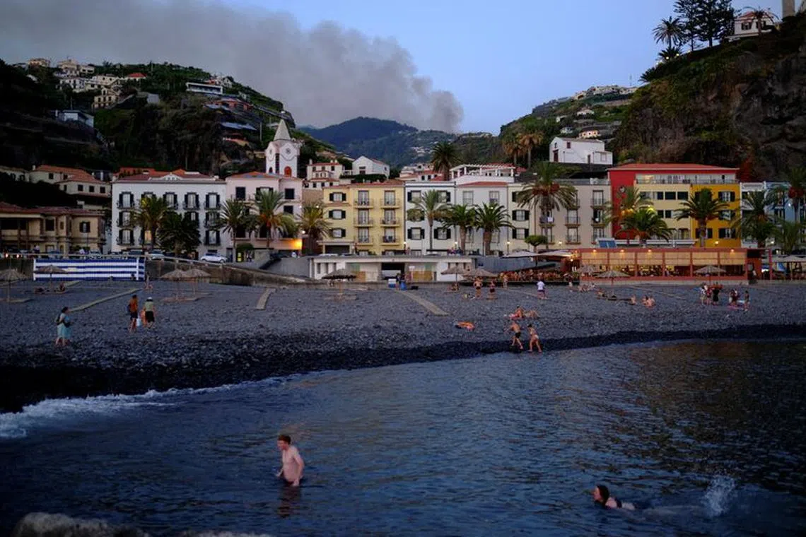 FILE PHOTO: Smoke from a wildfire is seen in the mountains of Portuguese island of Madeira as German tourists swim on the Atlantic at Ponta do Sol beach, Portugal October 5, 2023. REUTERS/Nacho Doce/File Photo