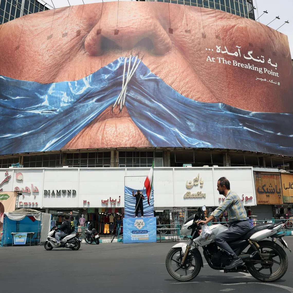 Iranians drive in front of a large anti-US billboard featuring US President Donald Trump and the Strait of Hormuz in Tehran.
