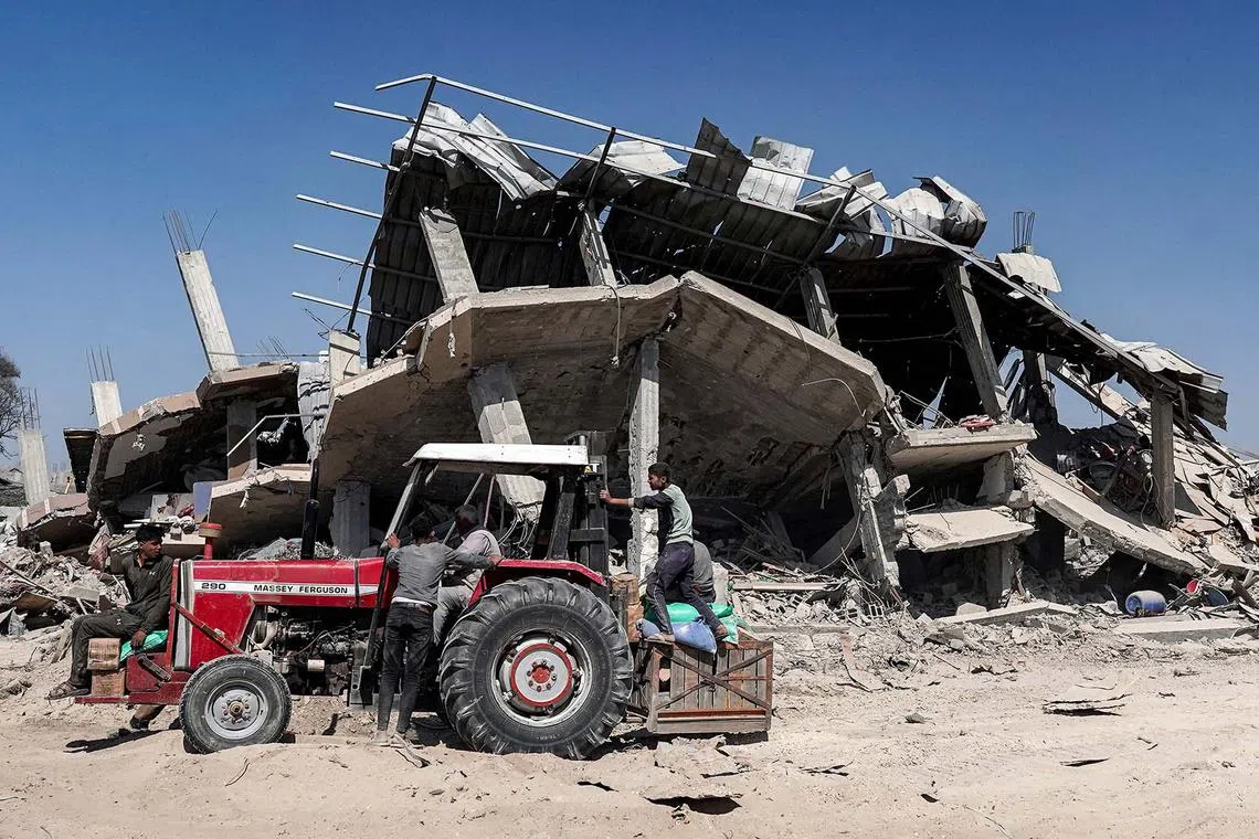People riding on a tractor picking up salvaged items from a damaged building in Khan Yunis on April 7, 2024 after Israel pulled its ground forces out of the southern Gaza Strip, six months into the devastating war sparked by the October 7 attacks. 