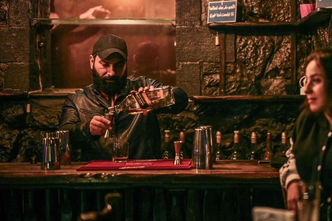 A pub owner serves whiskey to customers in Damascus.