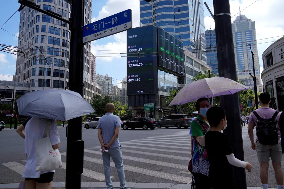 FILE PHOTO: Pedestrians wait to cross a road at a junction near a giant display of stock indexes in Shanghai, China August 3, 2022. REUTERS/Aly Song/File Photo
