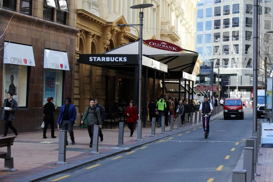 FILE PHOTO: People walk outside a Starbucks cafe on Lambton Quay street in Wellington, New Zealand. With economic momentum falling, interest rates rising and inflation cutting into household budgets, critics will seek to place the blame at Ardern's door.
