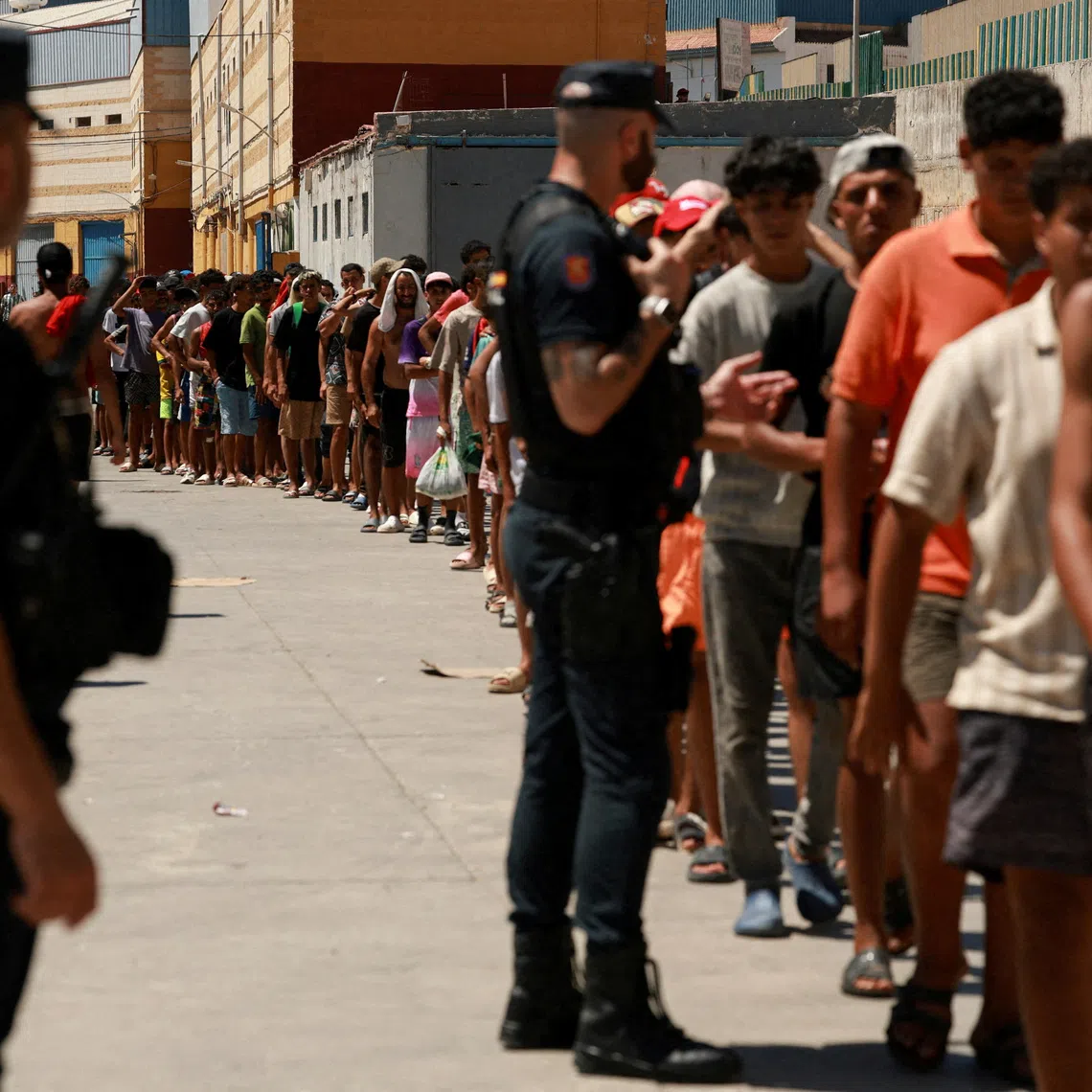 FILE PHOTO: Migrants queue to receive food staples from local NGO Media Luna Blanca in an industrial area where they are sleeping amid recent mass crossings by migrants on foot and by sea from Morocco into the Spanish territory, in Ceuta, Spain, August 6, 2026. REUTERS/Violeta Santos Moura/File Photo