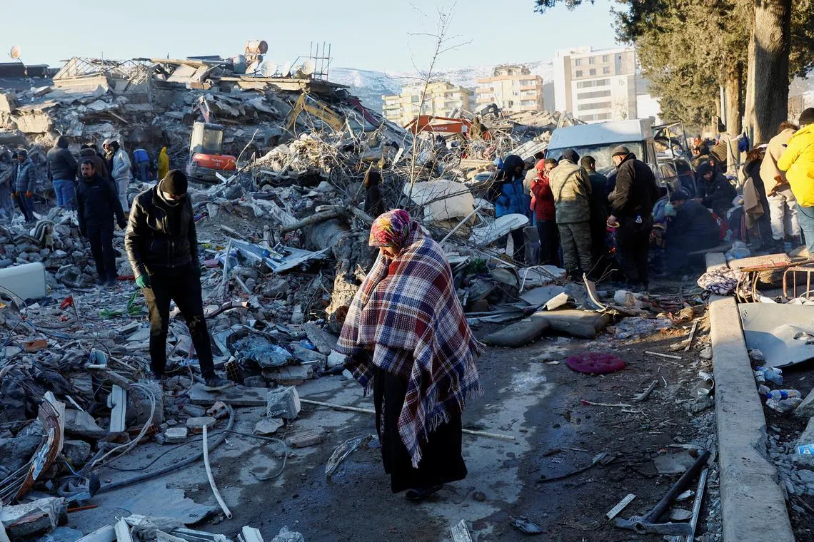 A woman stands near rubble and damages near the site of a collapsed buidling in the aftermath of an earthquake, in Kahramanmaras, Turkey, February 8, 2023. REUTERS/Suhaib Salem