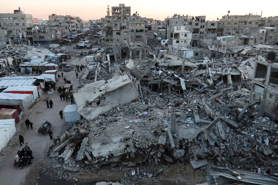 Palestinians walk among the rubble of buildings, amid a ceasefire between Israel and Hamas, in Khan Younis, in the southern Gaza Strip, February 27, 2025. REUTERS/Ramadan Abed