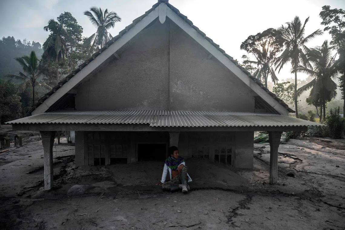A man sits in front of a house inundated by mud following a volcanic eruption by Mount Semeru at Kajar Kuning village in Lumajang on December 5, 2022. 