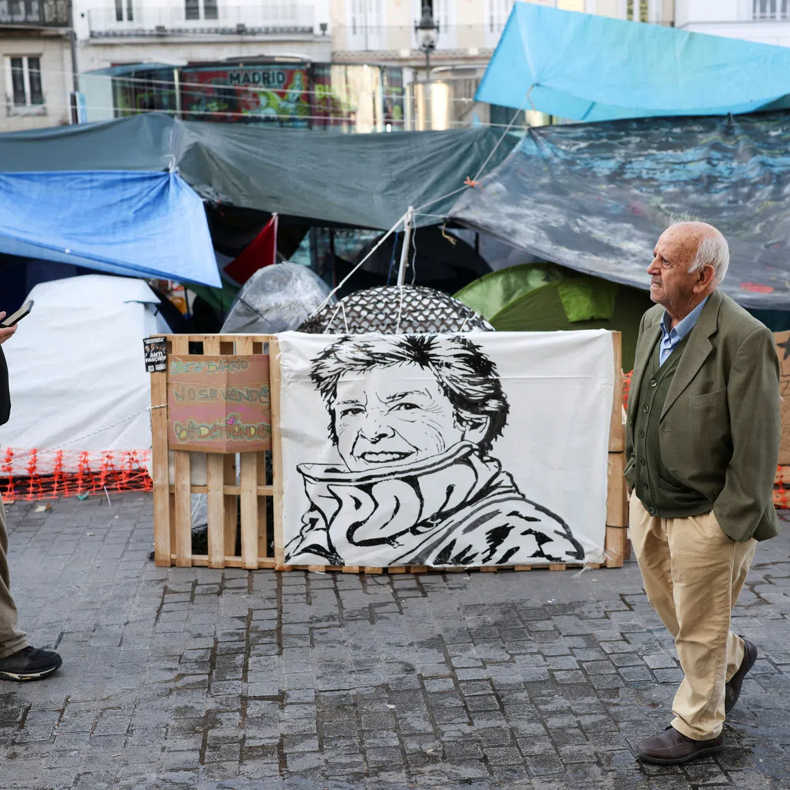 FILE PHOTO: People walk past a sign with the face of the late Maricarmen Abascal, an 87-year-old woman whose eviction sparked housing protests in Spain, at the protest camp at Puerta del Sol square in Madrid, Spain, October 10, 2026. REUTERS/Alejandro Martinez Velez/File Photo