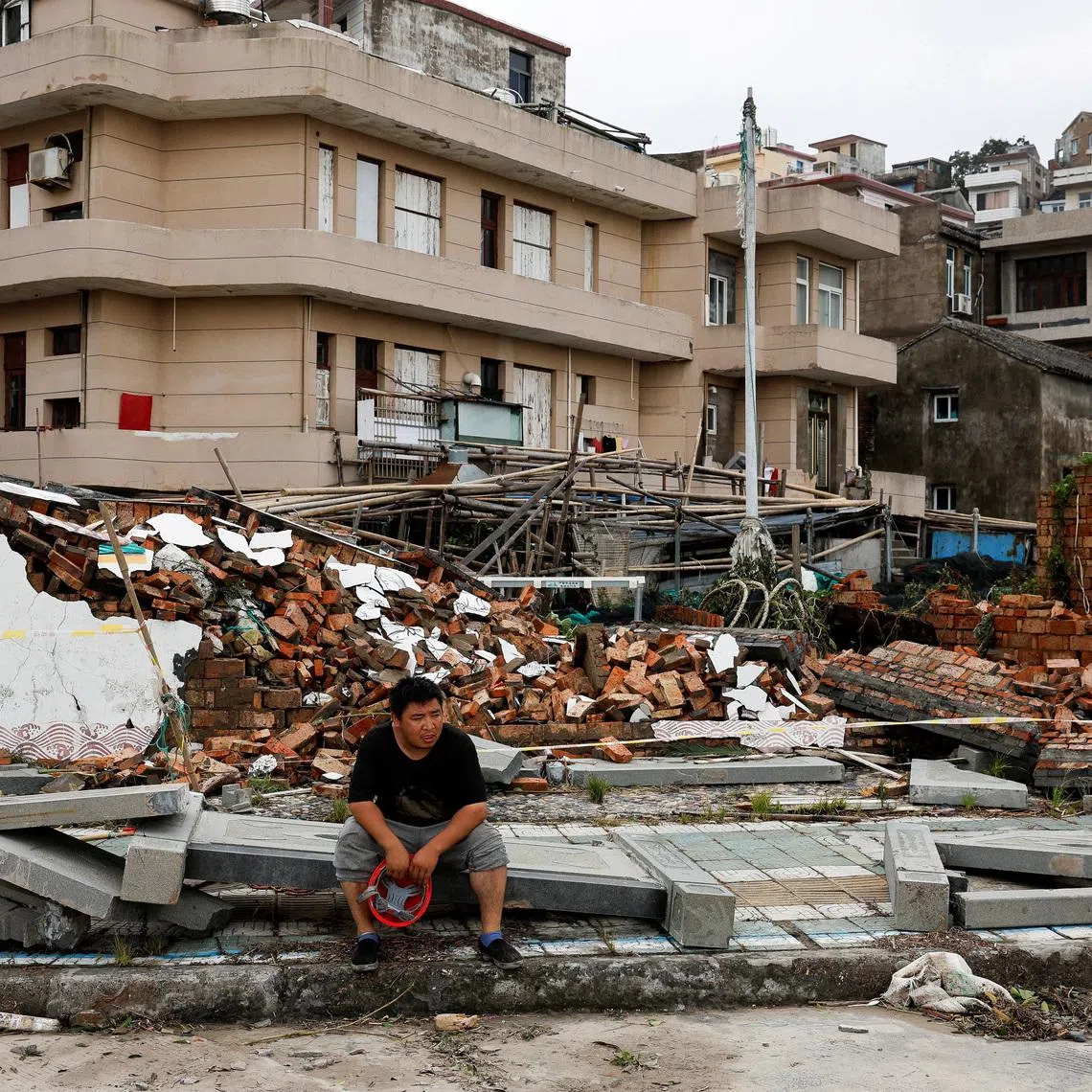 A person sits beside a collapsed wall in the aftermath of Typhoon Bavi in the coastal village of Dongsha, Taizhou, Zhejiang province, China, July 12, 2026. REUTERS/Go Nakamura