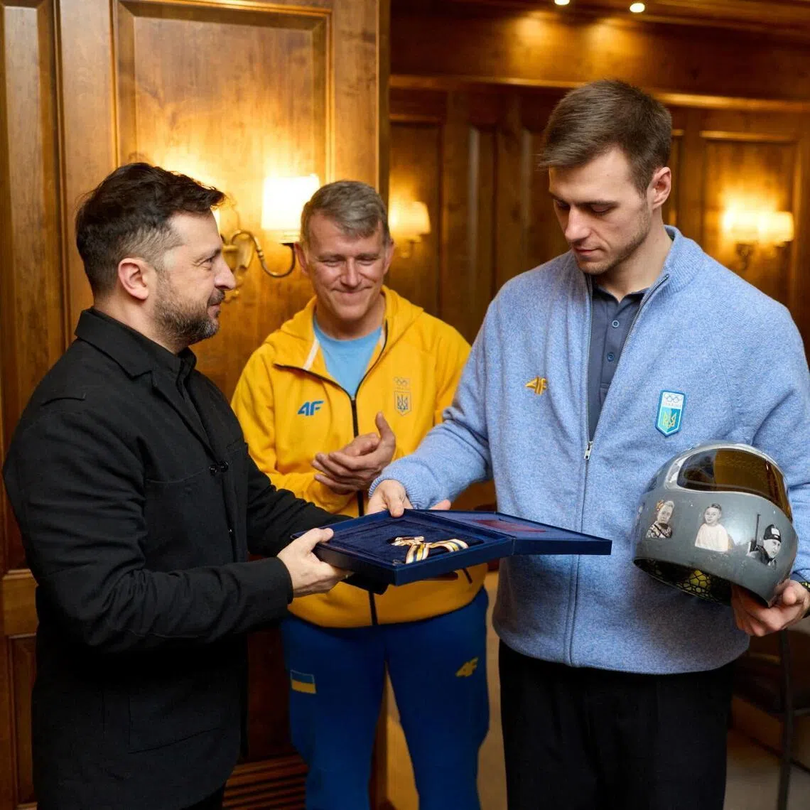 Ukrainian President Volodymyr Zelenskiy awards a medal of freedom on Feb 13, 2026 in Munich, Germany to Vladyslav Heraskevych, who was disqualified from the Olympic skeleton competition over his "helmet of remembrance" depicting athletes killed since Russia's invasion of Ukraine in 2022. Looking on is the racer's father and coach, Mykhailo. 