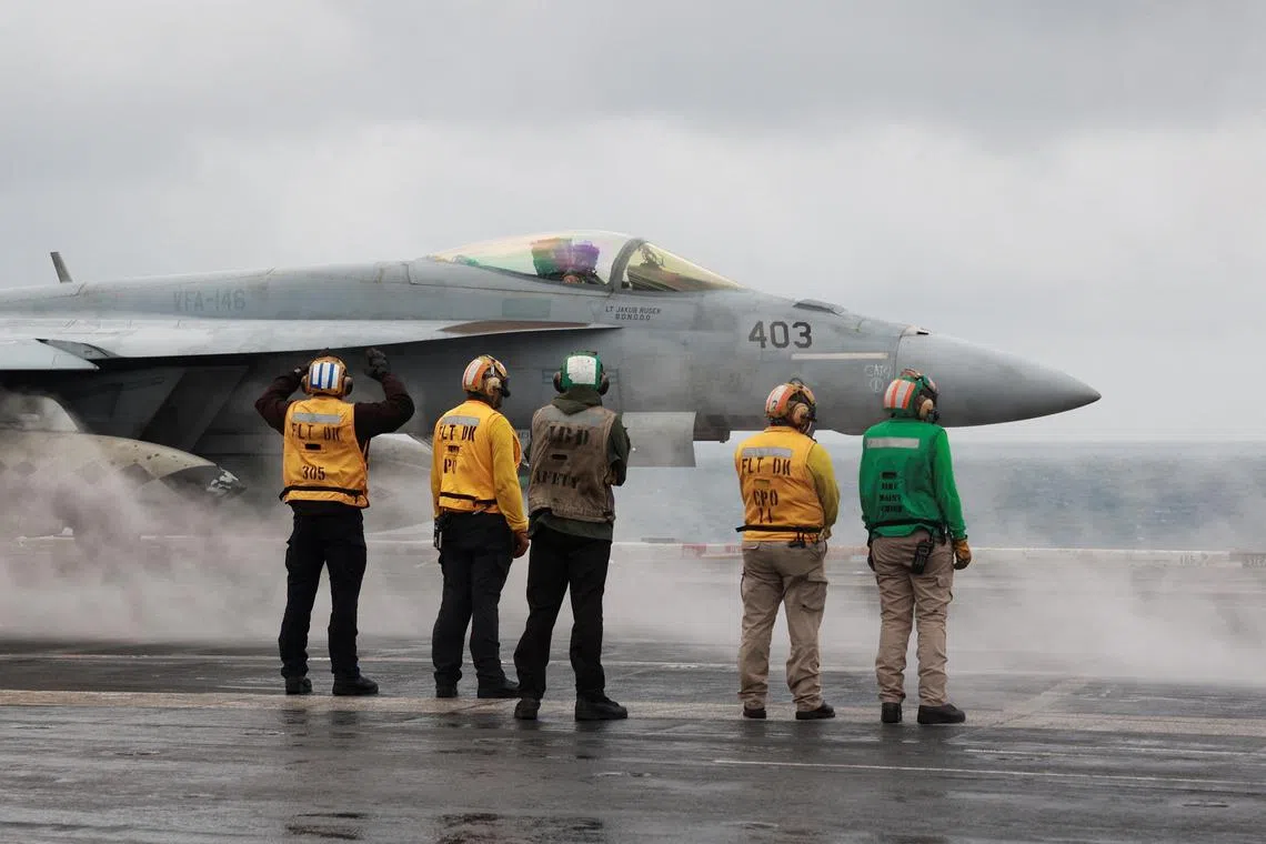 Crew members signal to an F/A-18E Super Hornet fighter jet preparing to take off for a routine flight, on board the USS Nimitz aircraft carrier in the South China Sea, on Jan 27, 2023.