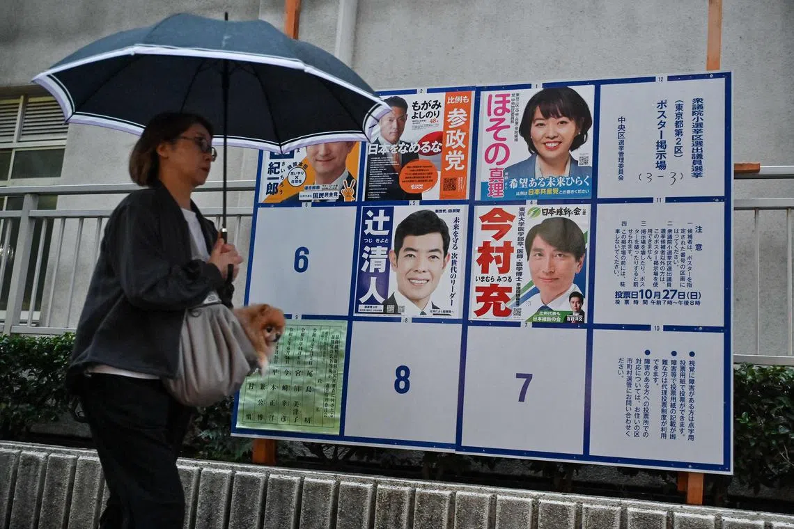 This photo taken on October 29, 2024 shows a pedestrian walking past a billboard displaying campaign posters for the country's recent general election, along a street in Tokyo. New lawmaker Saria Hino takes her seat on November 11 as one of a record number of women in Japan's parliament, but while campaigning ahead of the recent election, a voter asked her: "Who's looking after your children?" The mother-of-four was among 73 women elected to the 465-seat house of representatives in October's vote -- the most ever, but still a small minority at 16 percent. (Photo by Richard A. Brooks / AFP) / To go with 'JAPAN-POLITICS-VOTE-WOMEN-GENDER, FOCUS' by Kyoko HASEGAWA