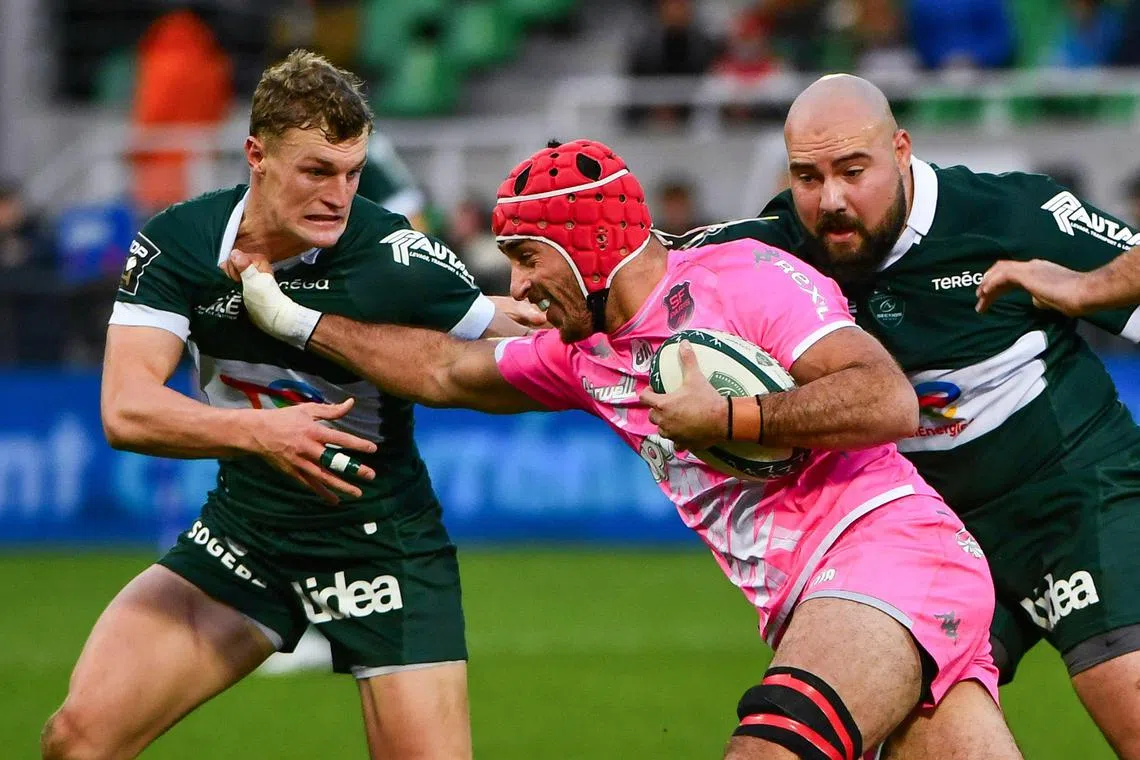 Stade Francais flanker Mathieu Hirigoyen, with protective head gear and mouthguard on, runs with the ball next to Pau centre Emilien Gailleton (left) during their French Top 14 rugby union match.