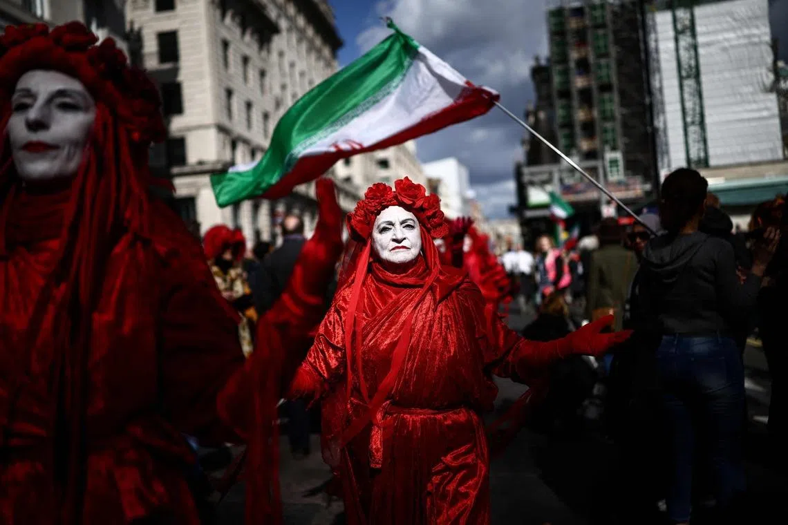 Members of the 'Red Rebel Brigade', a climate activist group, walking past Iranian flags being displayed as they join a march against the far right, organised by the Together Alliance, in central London, England on March 28, 2026. 