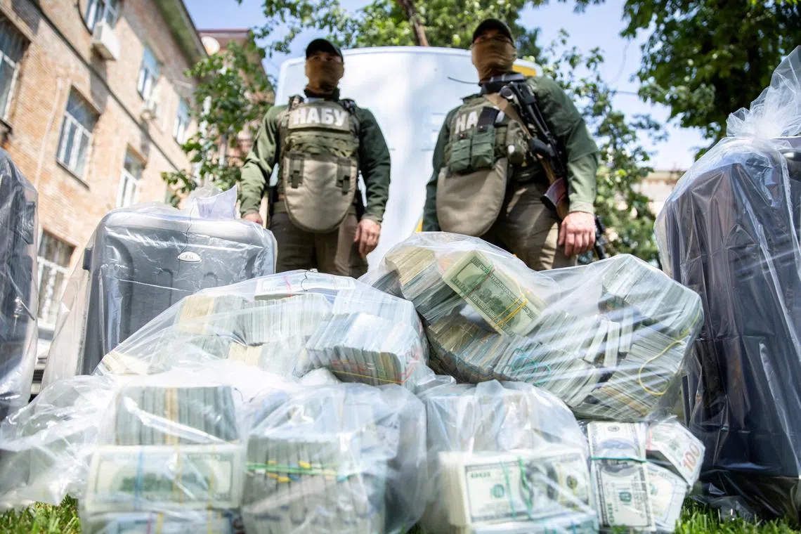 Officers of the National Anti-Corruption Bureau of Ukraine stand next to plastic bags filled with seized U.S. Dollar banknotes in Kiev, Ukraine, in this handout picture released June 13, 2020. Press Service of the National Anti-Corruption Bureau of Ukraine/Handout via REUTERS/File Photo