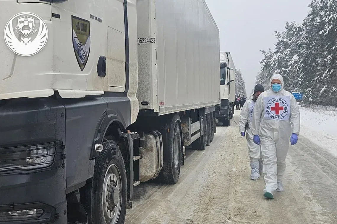 Employees walk past refrigerator trucks carrying what is reported to be the bodies of Ukrainian military personnel returned by Russia.