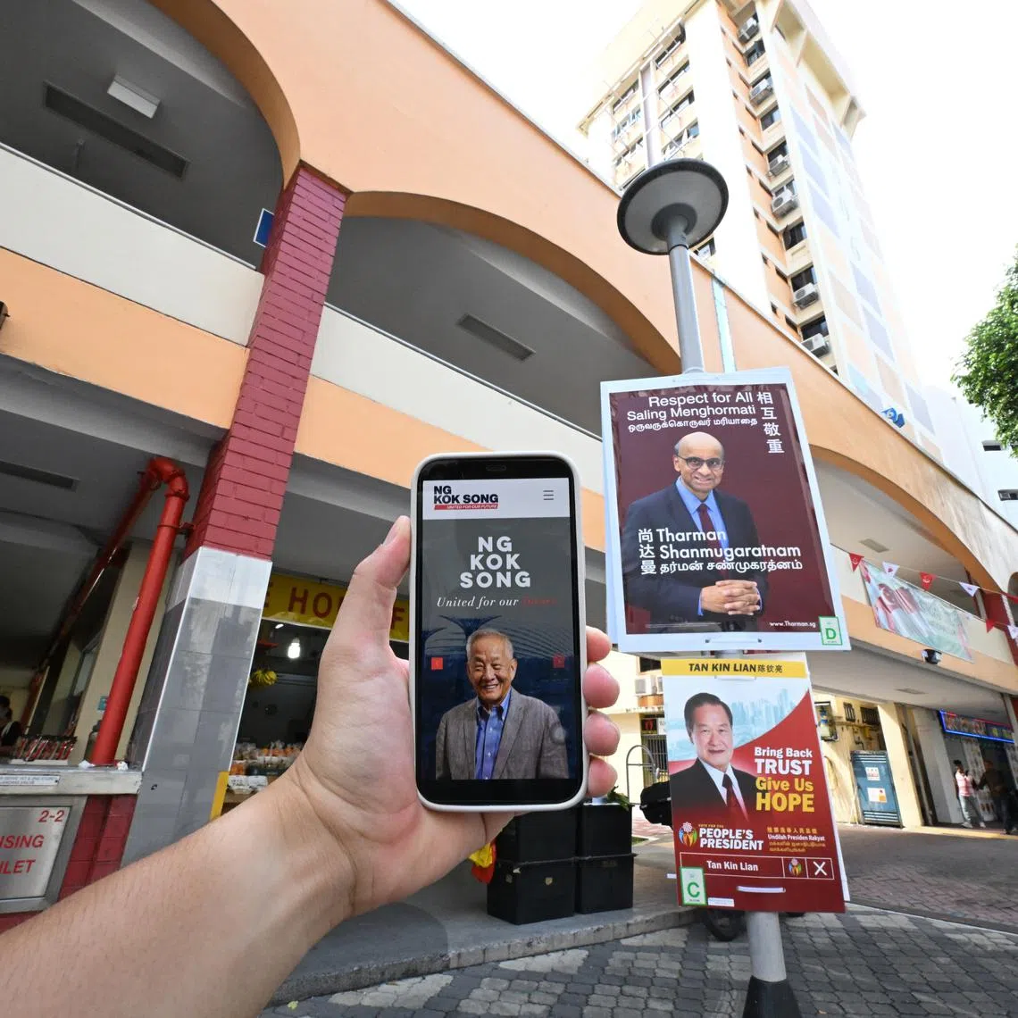 Posters of two presidential candidates Tharman Shanmugaratnam Tan Kin Lian, and a phone with a a screenshot of Mr Ng Kok Song's website at French Road on Aug 29, 2023.