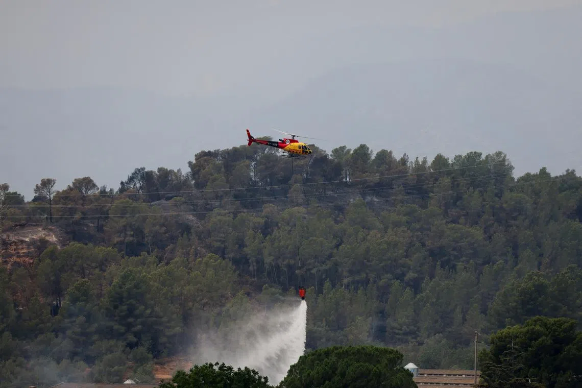 A helicopter helps to extinguish an ongoing wildfire in Xerta, which is one of the confined villages in the Tarrragona province in Catalonia, Spain, July 8, 2025. REUTERS/Nacho Doce