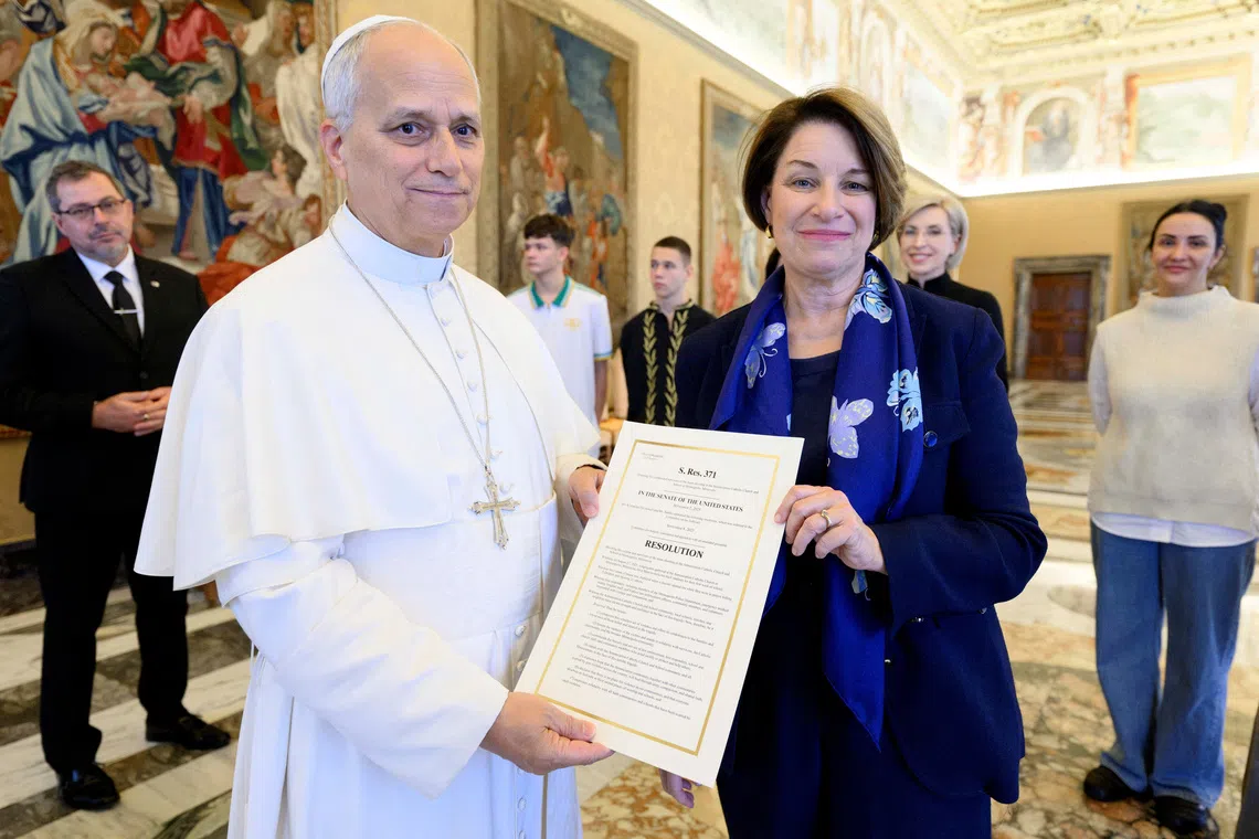 Pope Leo XIV and U.S. Senator Amy Klobuchar (D-MN) pose for a photo with a copy of a U.S. Senate bill commemorating the victims of the shooting at a Minnesota Catholic church and school, at the Vatican, November 21, 2025. Simone Risoluti/Vatican Media/­Handout via REUTERS