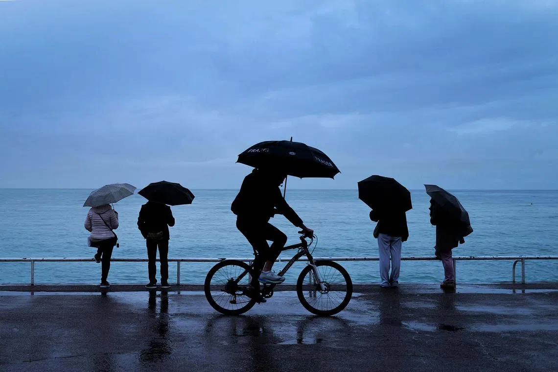 A man riding a bicycle with his umbrella during heavy rain on the Promenade des Anglais at the french riviera city of Nice, south-eastern France, on April 16, 2025. 