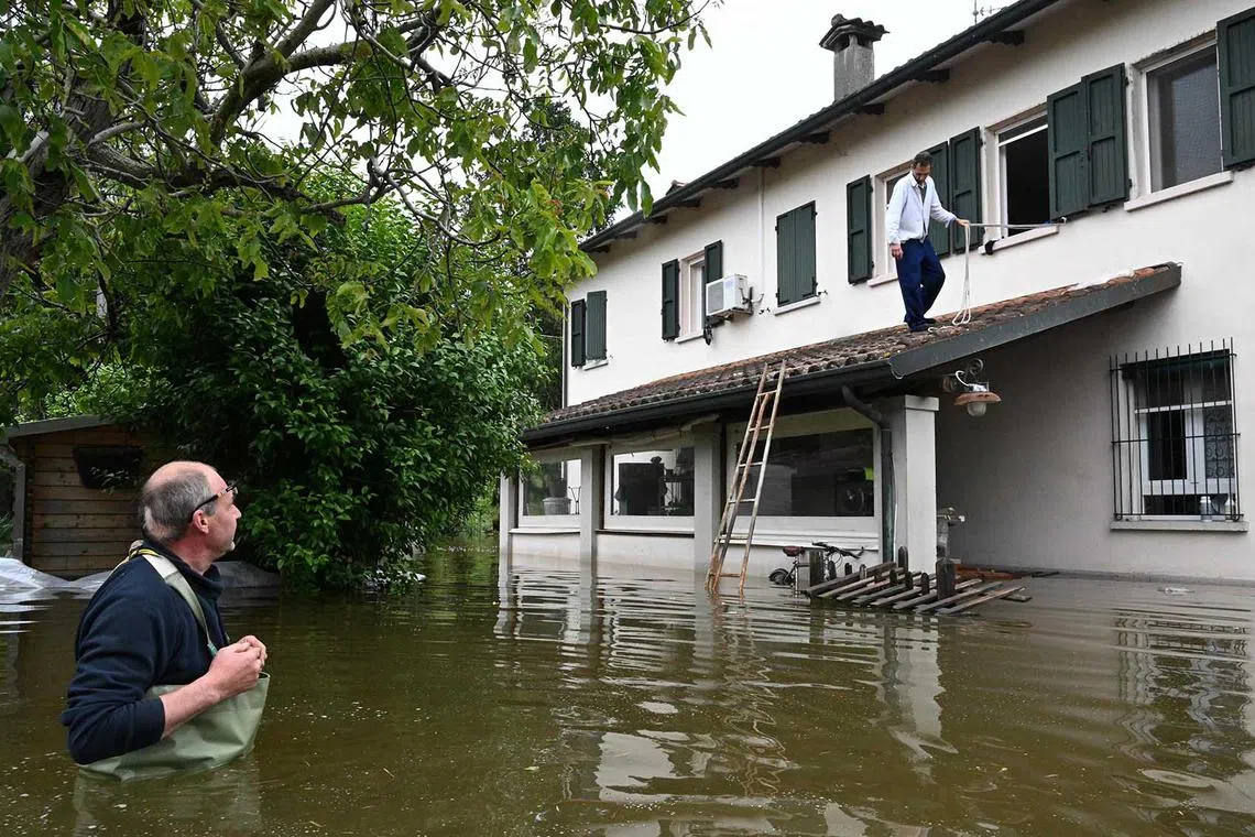 TOPSHOT - A man stranded in his flooded property (Top R) uses a rope and a ladder to get out as his cousin looks on, on May 20, 2023 in the village of Ghibullo, near Ravenna, after floodwaters hit the Emilia-Romagna region. The toll from floods that have devastated Italy's Emilia Romagna region rose to 14 on May 19, amid calls for the government to revive an abandoned project to mitigate the impact of natural disasters. (Photo by Andreas SOLARO / AFP)