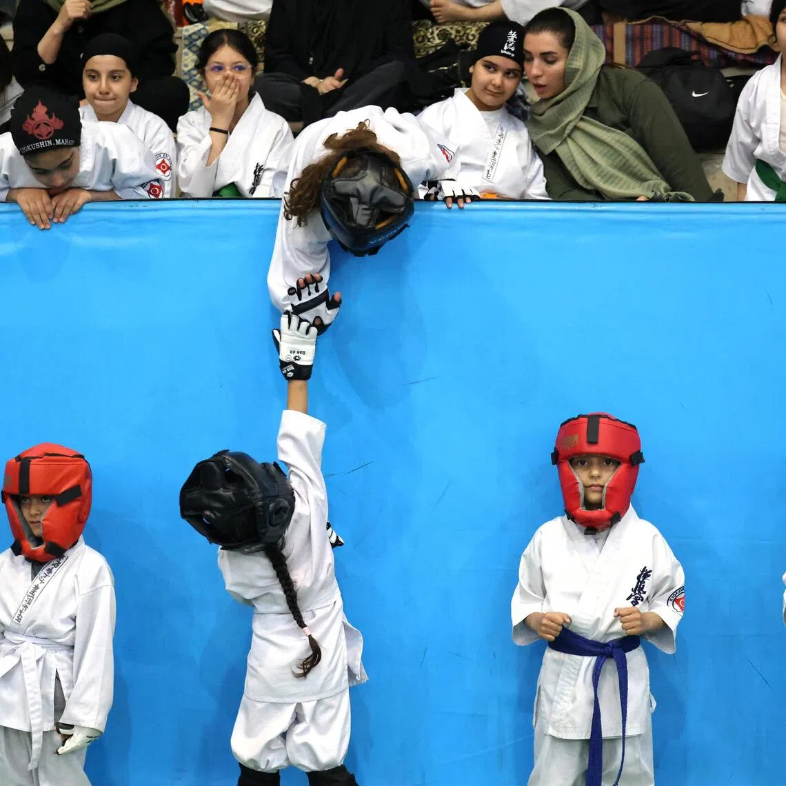 A young athlete reaches up to give a "high-five" during the women's karate competition, made-up of clubs and teams from around the Tehran province.