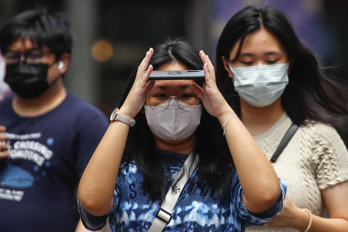 A woman covers her face with her phone during a hot day in Kuala Lumpur, Malaysia, April 27, 2023. 