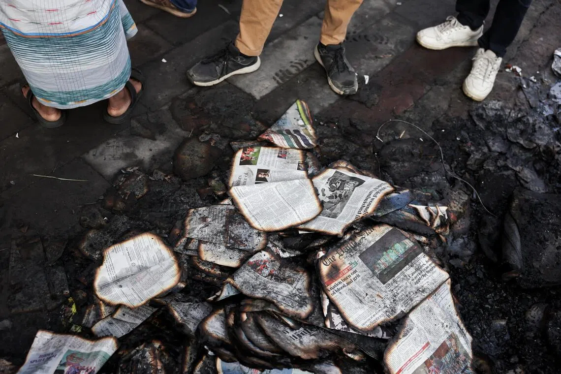People stand next to burnt newspapers in front of the Daily Star building, following the death of student leader Sharif Osman Hadi, in Dhaka, Bangladesh, on Dec 19, 2025.