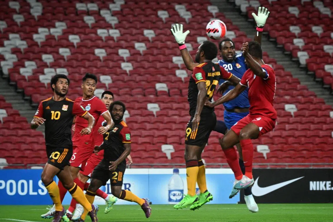 Papua New Guinea goalkeeper Ronald Warisan (in blue) and defender Joshua Talau in an aerial challenge with Singapore captain Hariss Harun, as fellow Lions Amirul Adli and Lionel Tan (in red) look on.