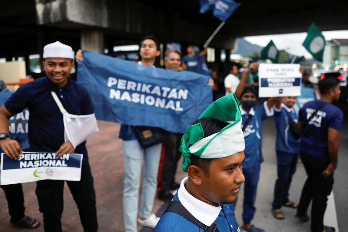 A Pan-Malaysian Islamic Party (PAS) supporter wraps his head with the party's flag as he campaigns for PAS' political coalition, Perikatan Nasional during the campaign period of Malaysia's general election at Permatang Pauh, Penang, Malaysia on Nov 18, 2022. 