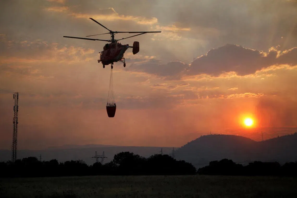 A firefighting helicopter flies over Rogami suburb during sunset, as temperature rises during a heatwave in Podgorica, Montenegro, Aug 11, 2025.