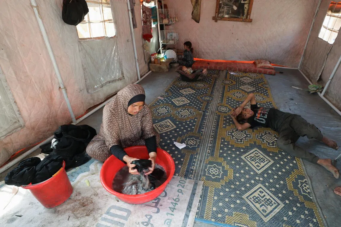 Palestinian woman, Mervat Hijazi, washes clothes inside the tent they took shelter after being displaced, in Gaza City, May 22, 2025. REUTERS/Mahmoud Issa
