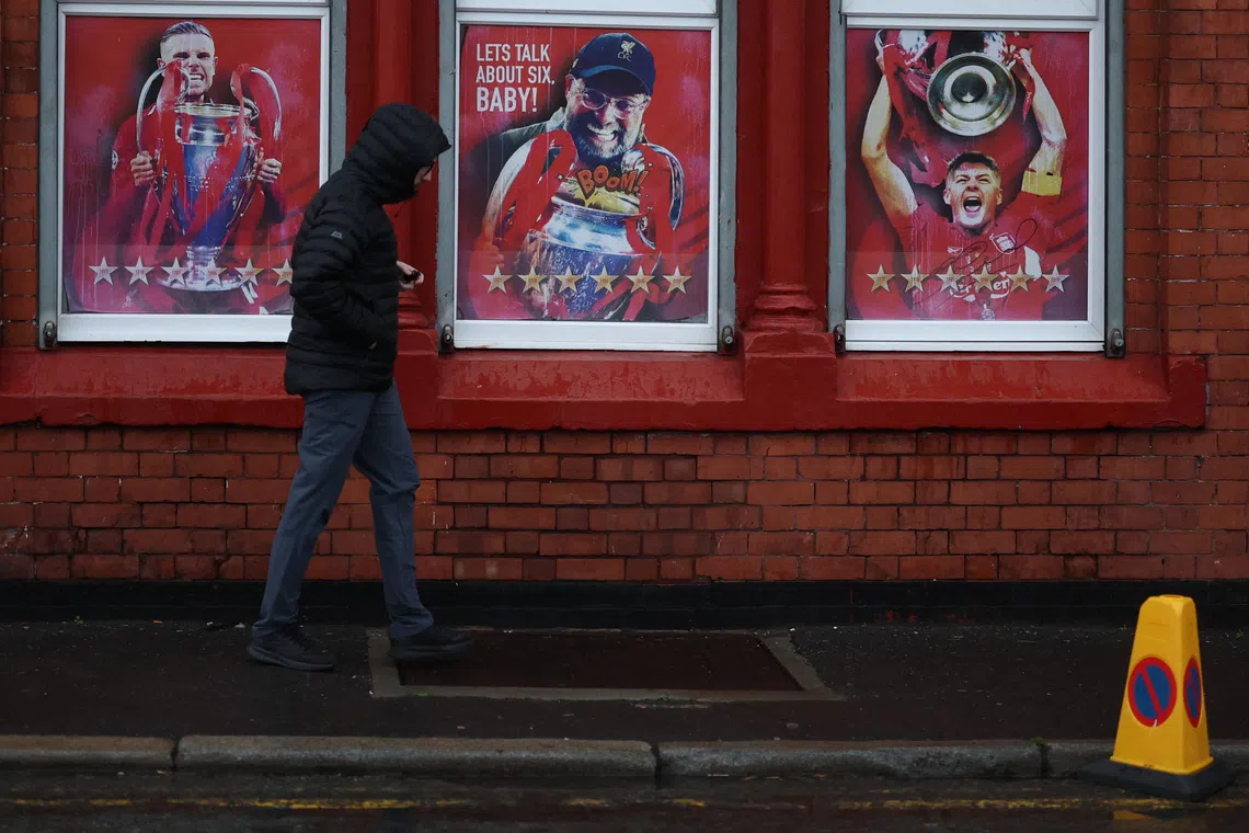 Soccer Football - Premier League - Liverpool v Manchester United - Anfield, Liverpool, Britain - October 19, 2025 General view as a fan walks past posters of former Liverpool manager Juergen Klopp and players Jordan Henderson and Steven Gerrard lifting the Champions League trophy outside the stadium before the match REUTERS/Phil Noble